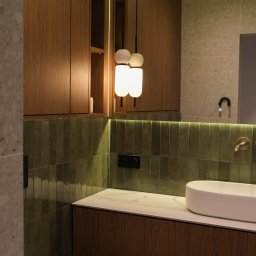 Wiktoria Surgota Moono Design - Nowoczesna łazienka z drewnianymi szafkami, zielonymi płytkami i okrągłą lampą. Umywalka nablatowa i bateria w kolorze złota. Minimalistyczny design.