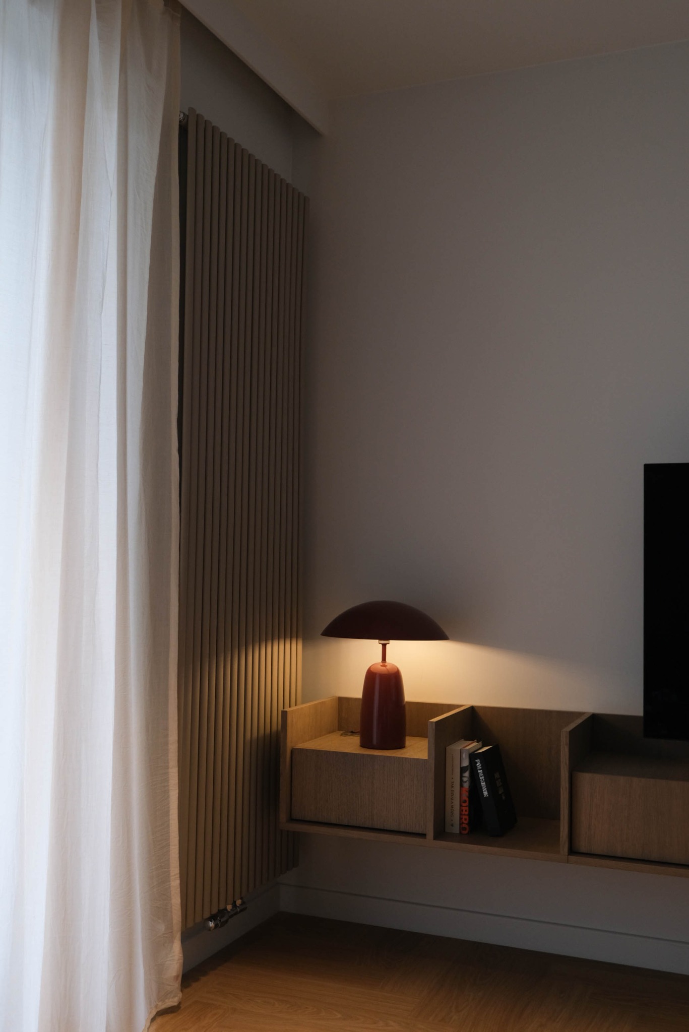 Nowoczesny salon: beżowe lamele ścienne, zwiewna firana i podświetlana, minimalistyczna szafka RTV z czerwoną lampką. Subtelne oświetlenie tworzy przytulny klimat.