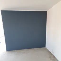 Wnętrze pokoju po malowaniu jednej ściany na ciemny grafit, widoczne kable elektryczne przy podłodze, surowa podłoga przed wykończeniem.