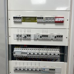 ElektroCare - Rozdzielnica elektryczna z zabezpieczeniami nadprądowymi, wyłącznikami różnicowoprądowymi i ogranicznikiem przepięć w białej obudowie, widoczne okablowanie, etykiety opisujące obwody.