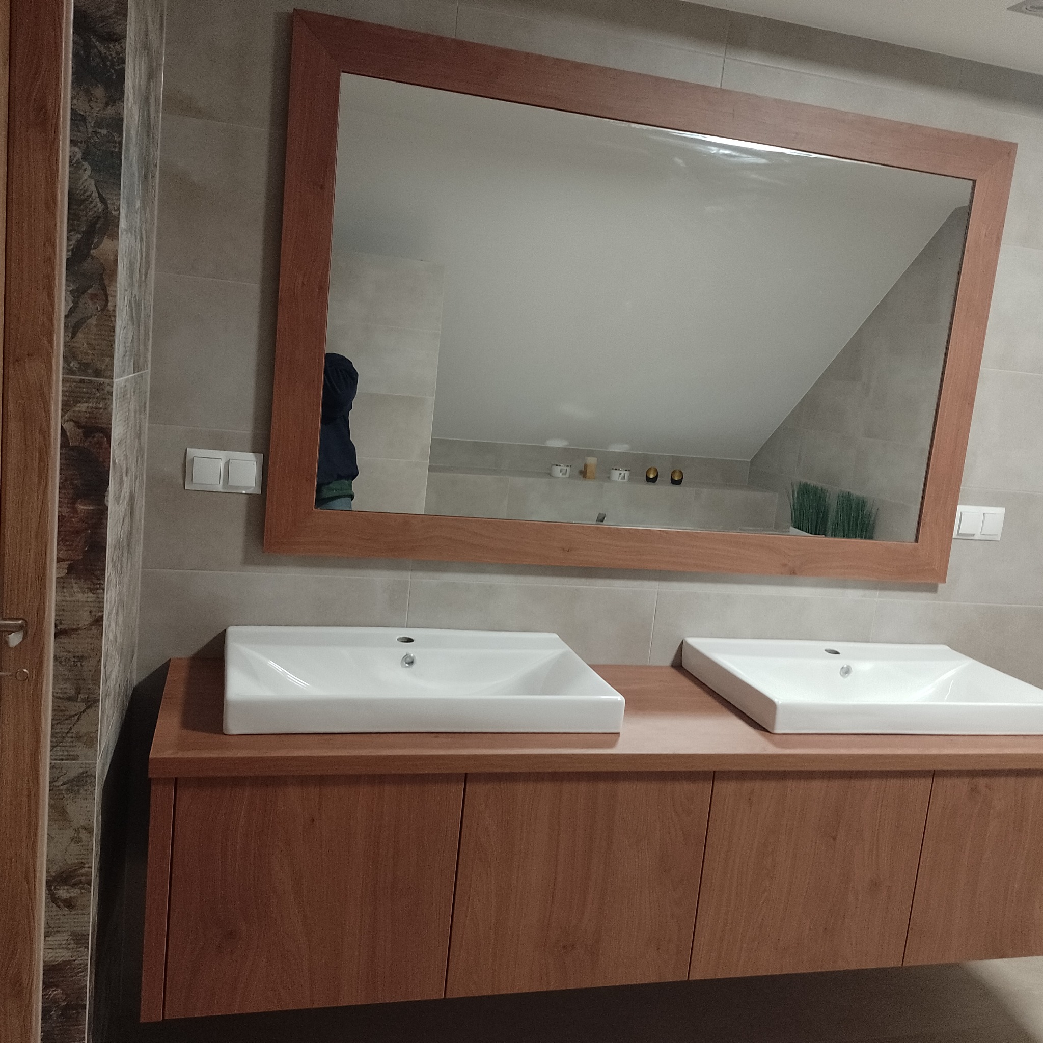 Łazienka z dwoma białymi umywalkami nablatowymi na drewnianej szafce, duże lustro w drewnianej ramie odbija fragment sufitu i dekoracje.