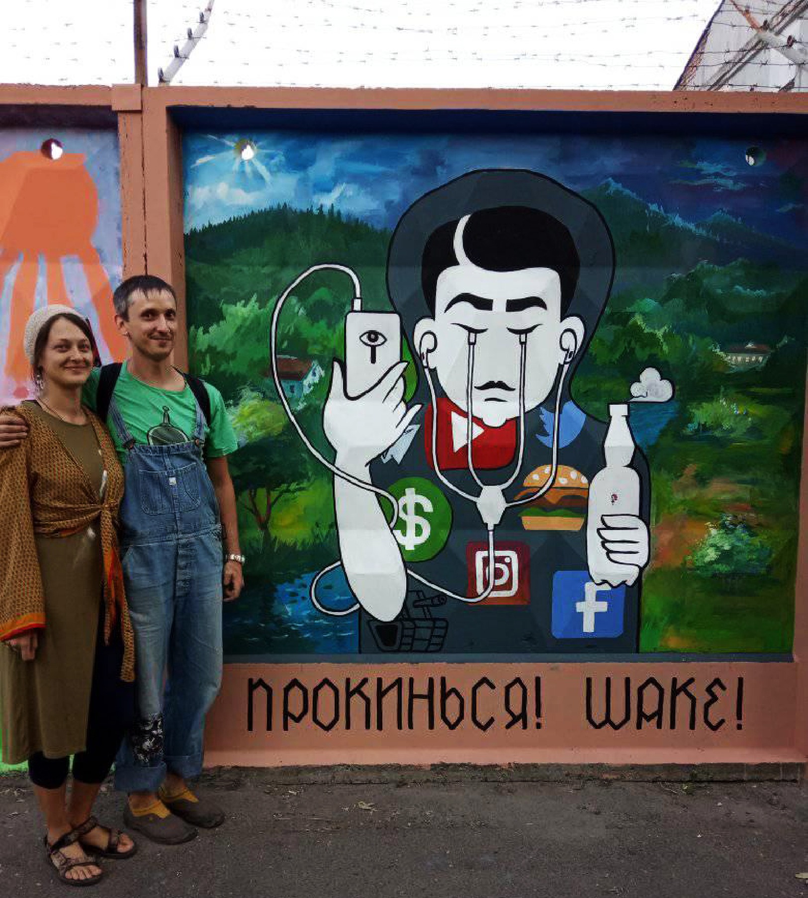Para pozuje przed muralem przedstawiającym postać z podłączonym telefonem, płaczącą ikonami aplikacji i trzymającą butelkę, na tle górskiego krajobrazu.