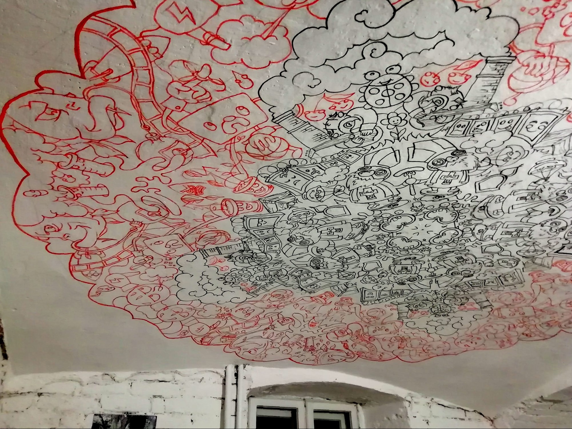Ilustracja na suficie przedstawiająca chaotyczny zbiór postaci i obiektów, z lewej strony wykonana czerwoną linią, a z prawej czarną, widok z dołu na fragment ściany z oknem.