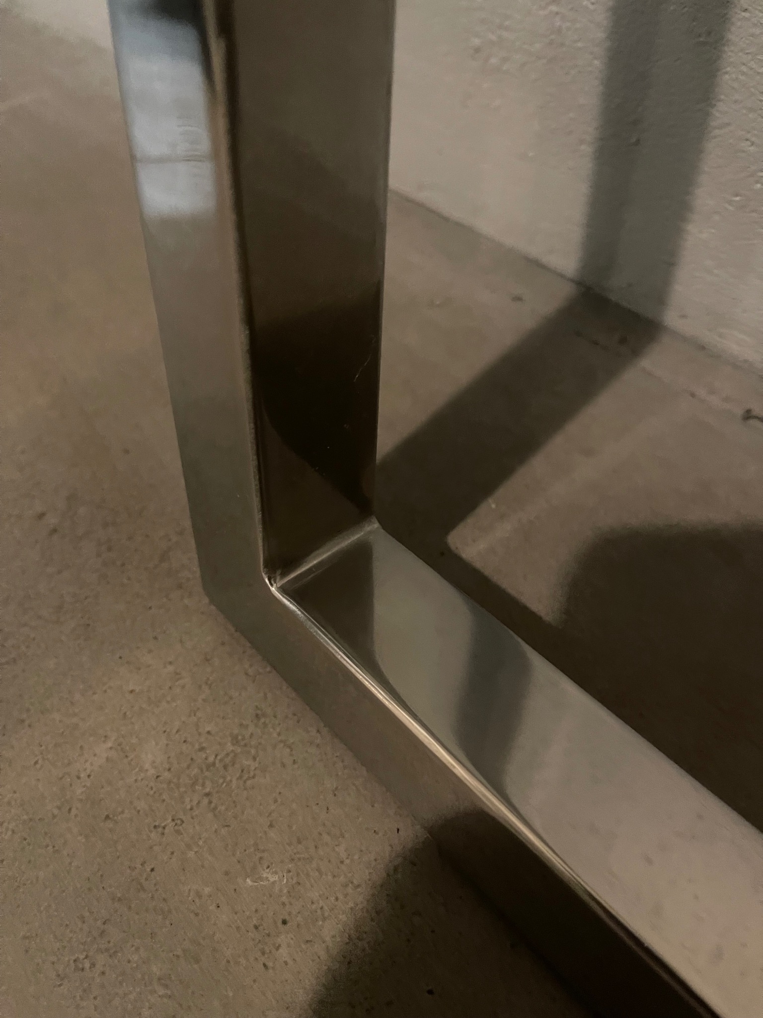 Fragment konstrukcji ze stali nierdzewnej w Szczecinie, prawdopodobnie elementu balustrady lub poręczy, z widocznym spawem i odbiciem światła na gładkiej powierzchni.