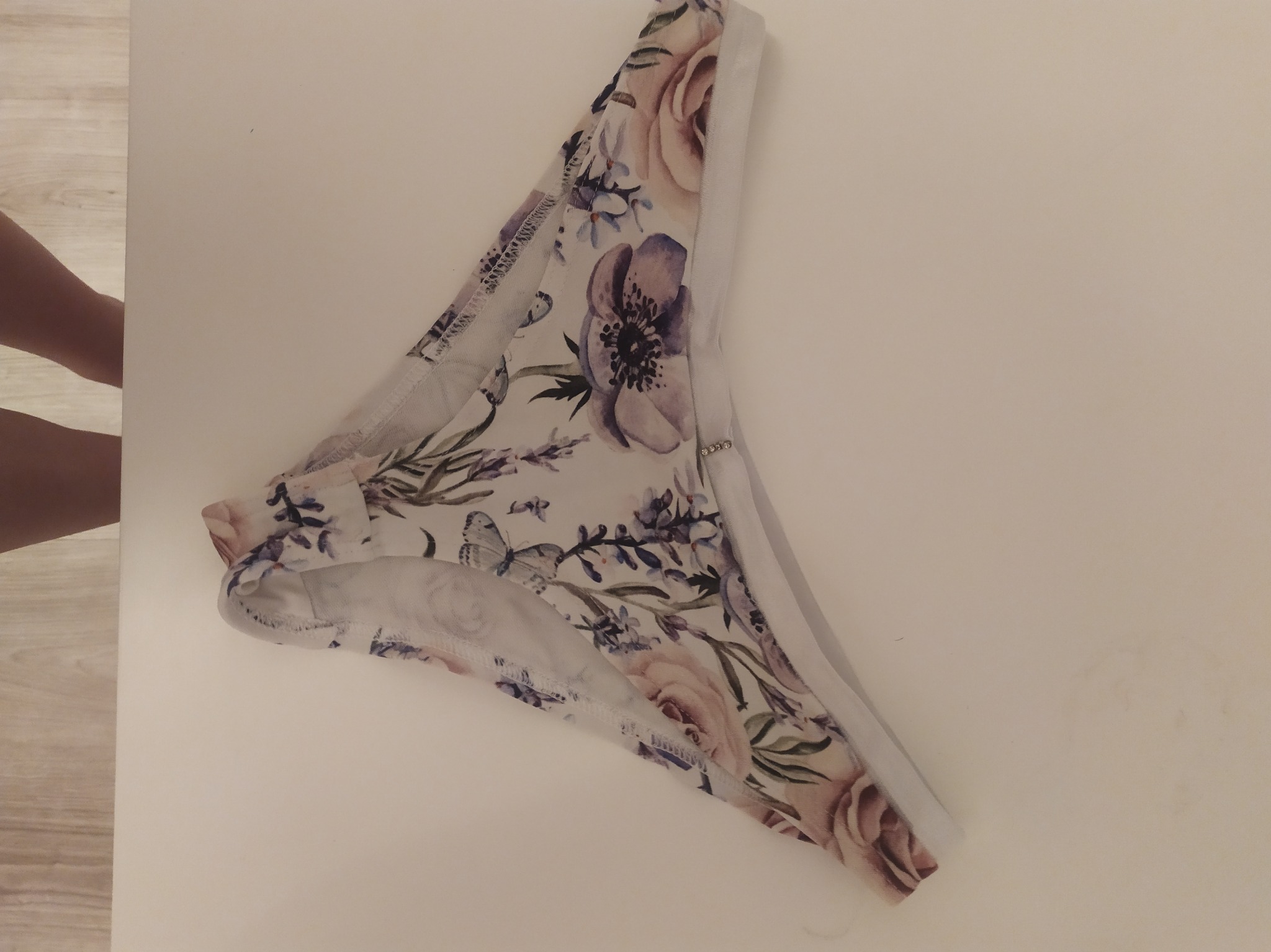 Damskie majtki typu figi z kwiatowym wzorem w odcieniach fioletu i różu, leżące na jasnym tle.