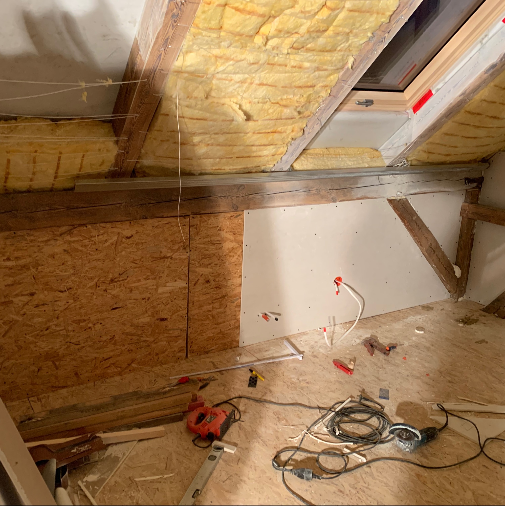 Poddasze w trakcie remontu: ocieplenie wełną mineralną poddasza, fragment ściany z płyty karton gips, widoczne przewody elektryczne i narzędzia budowlane na podłodze z płyt OSB.