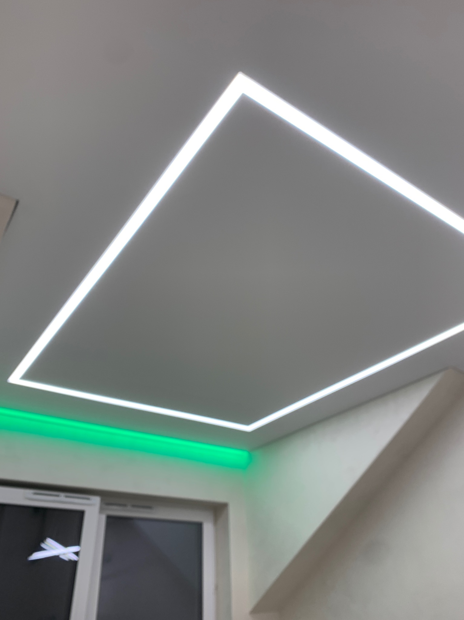 Biały sufit z wpuszczonym kwadratowym oświetleniem LED, dodatkowo podświetlenie LED w kolorze zielonym nad oknem.
