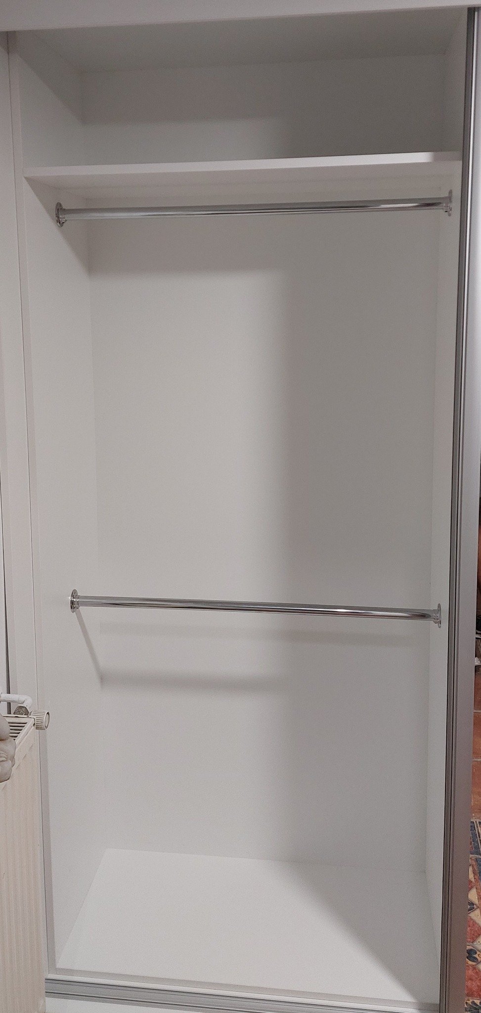 Wnętrze białej szafy wnękowej z dwoma chromowanymi drążkami na ubrania, widok z przodu, pusta przestrzeń do przechowywania.