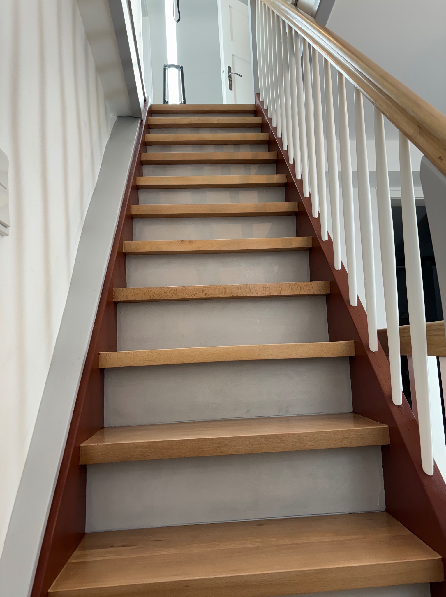 Jasne drewniane schody z szarymi podstopnicami i białymi balustradami, widok z dołu, nowoczesny design.