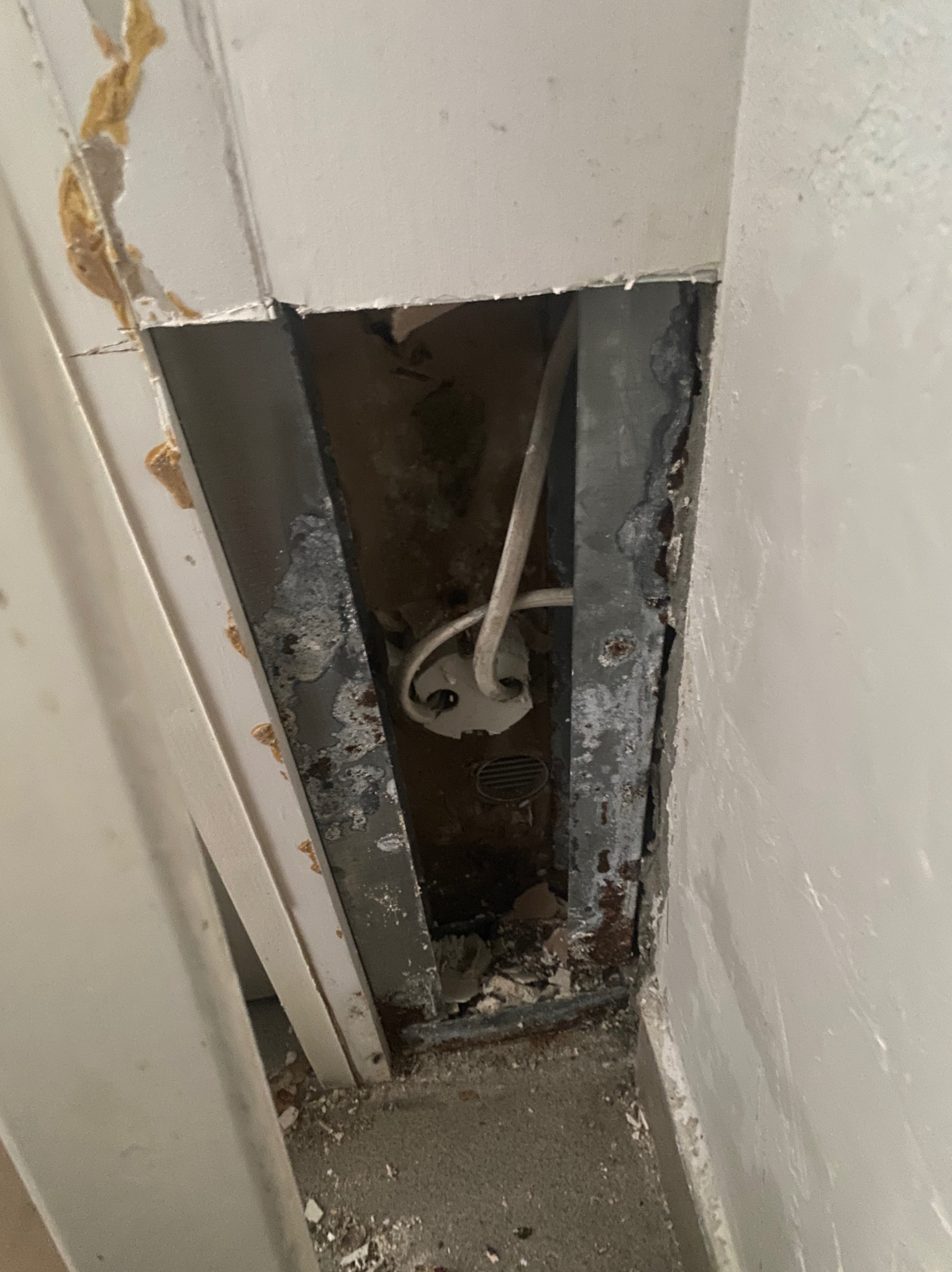 Otwór w ścianie odsłaniający instalację elektryczną z widocznymi przewodami i puszką podtynkową, zniszczone wykończenie ściany i widoczne ślady korozji.