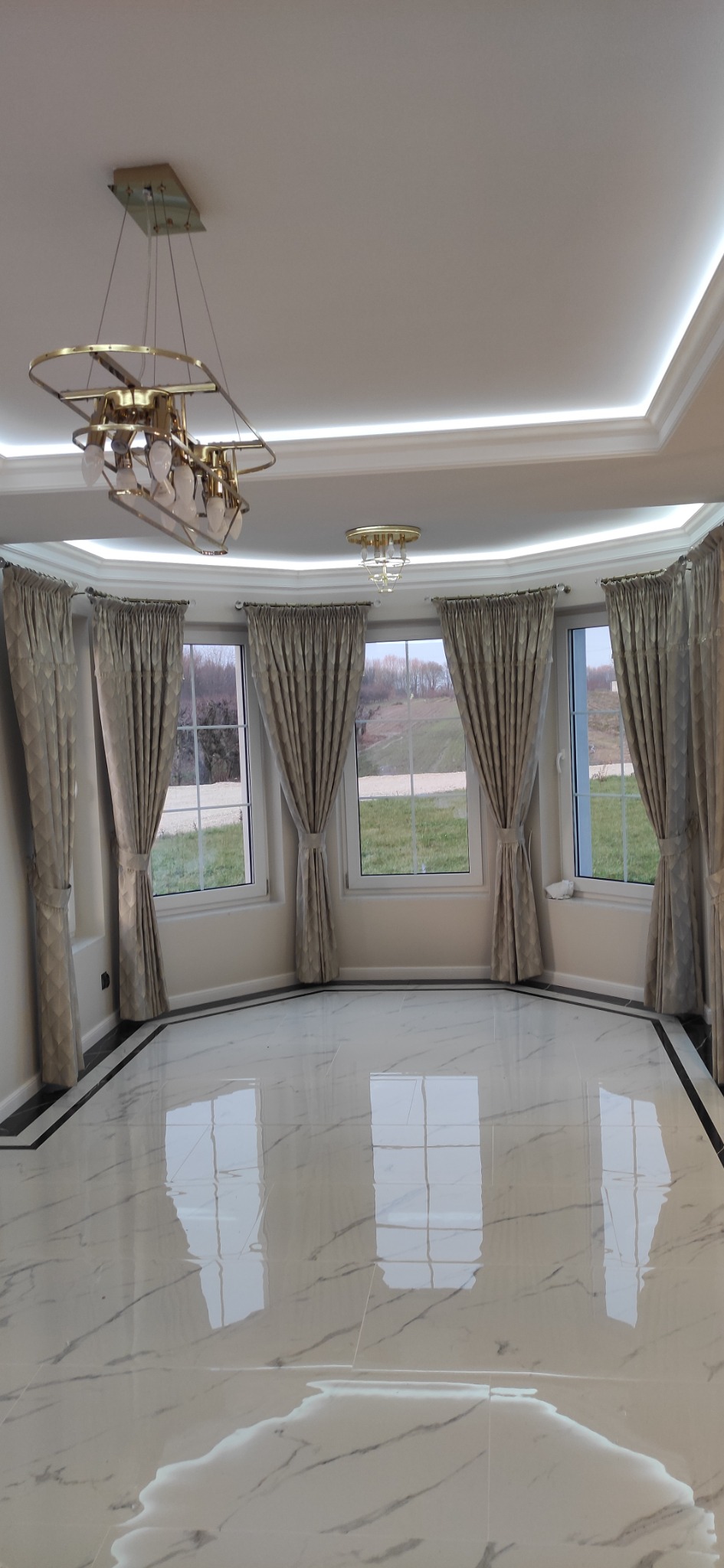 Eleganckie wnętrze z marmurową podłogą, oknami z zasłonami i nowoczesnym oświetleniem sufitowym, widok na zewnątrz z zielenią.