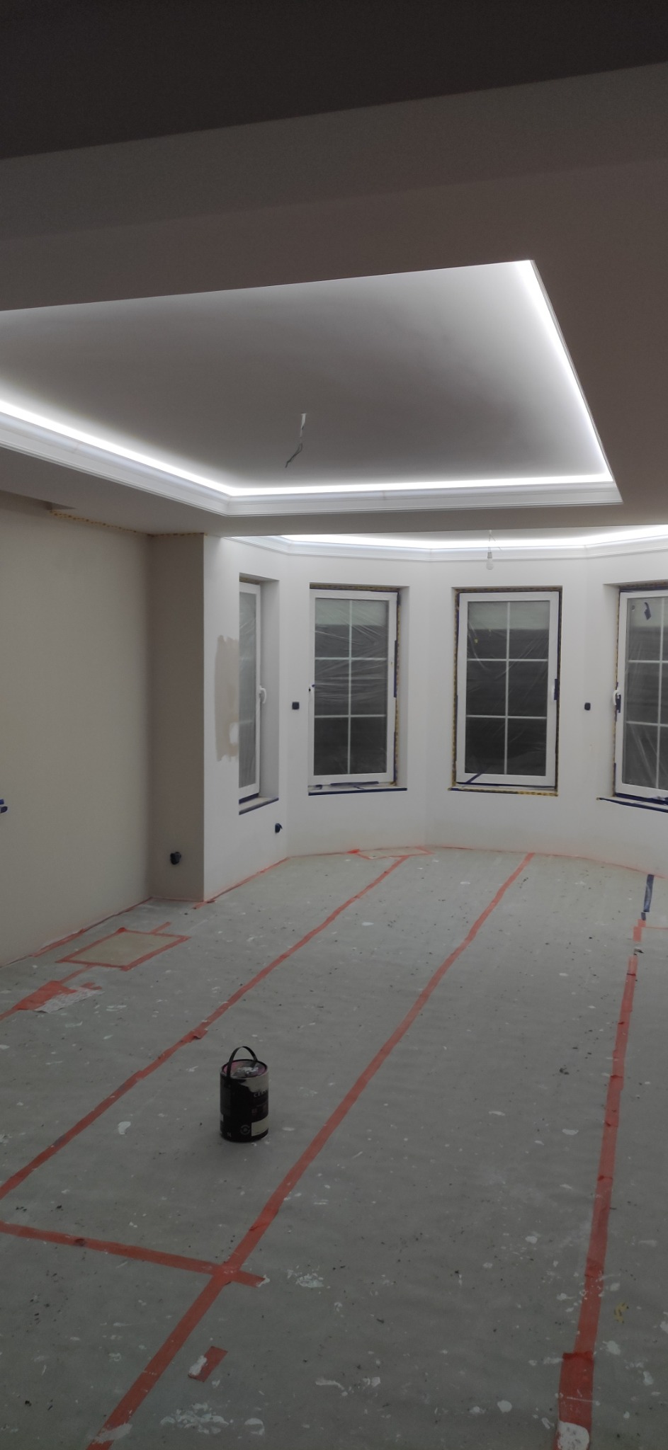 Przygotowane do malowania wnętrze z oświetleniem LED na suficie, zabezpieczoną podłogą taśmą malarską i puszką farby w rogu.