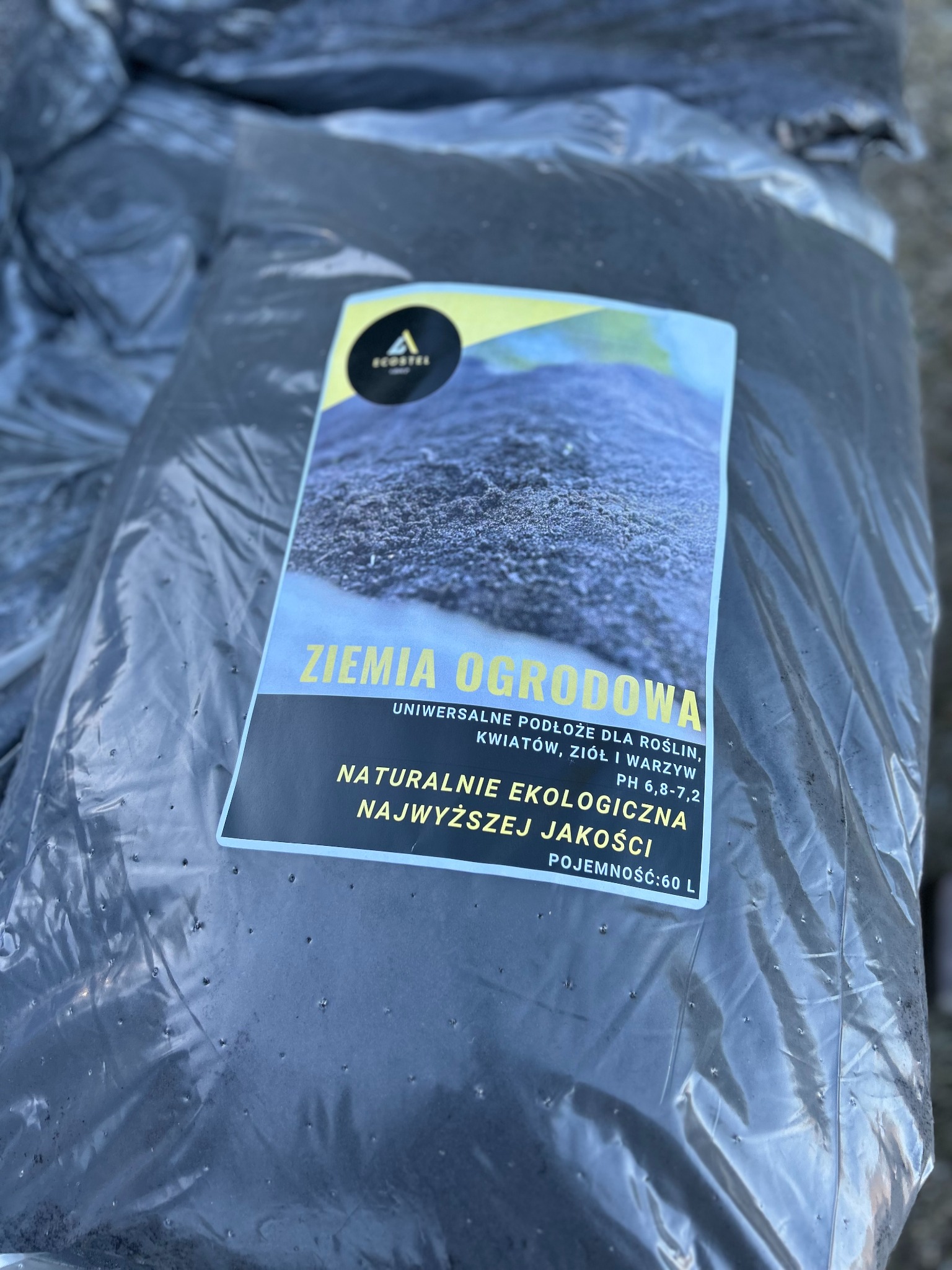 Worek z czarną ziemią ogrodową, z widoczną etykietą informującą o uniwersalnym zastosowaniu do roślin, kwiatów, ziół i warzyw, zapakowany w folię.
