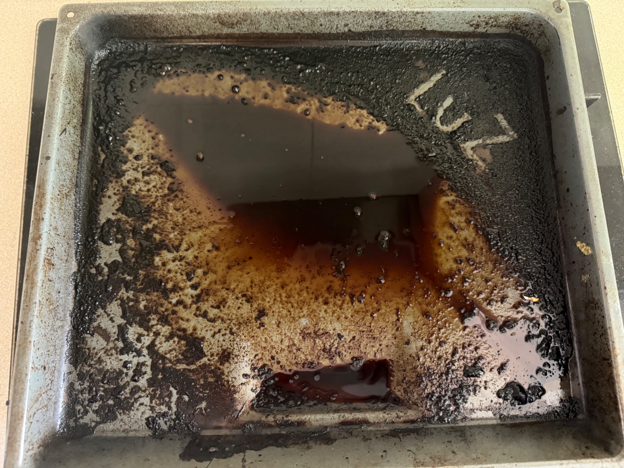 Zabrudzona blacha do pieczenia z przypalonym tłuszczem i resztkami jedzenia, widoczne osady i plamy. Wnętrze blachy wypełnione ciemną, lepką substancją.