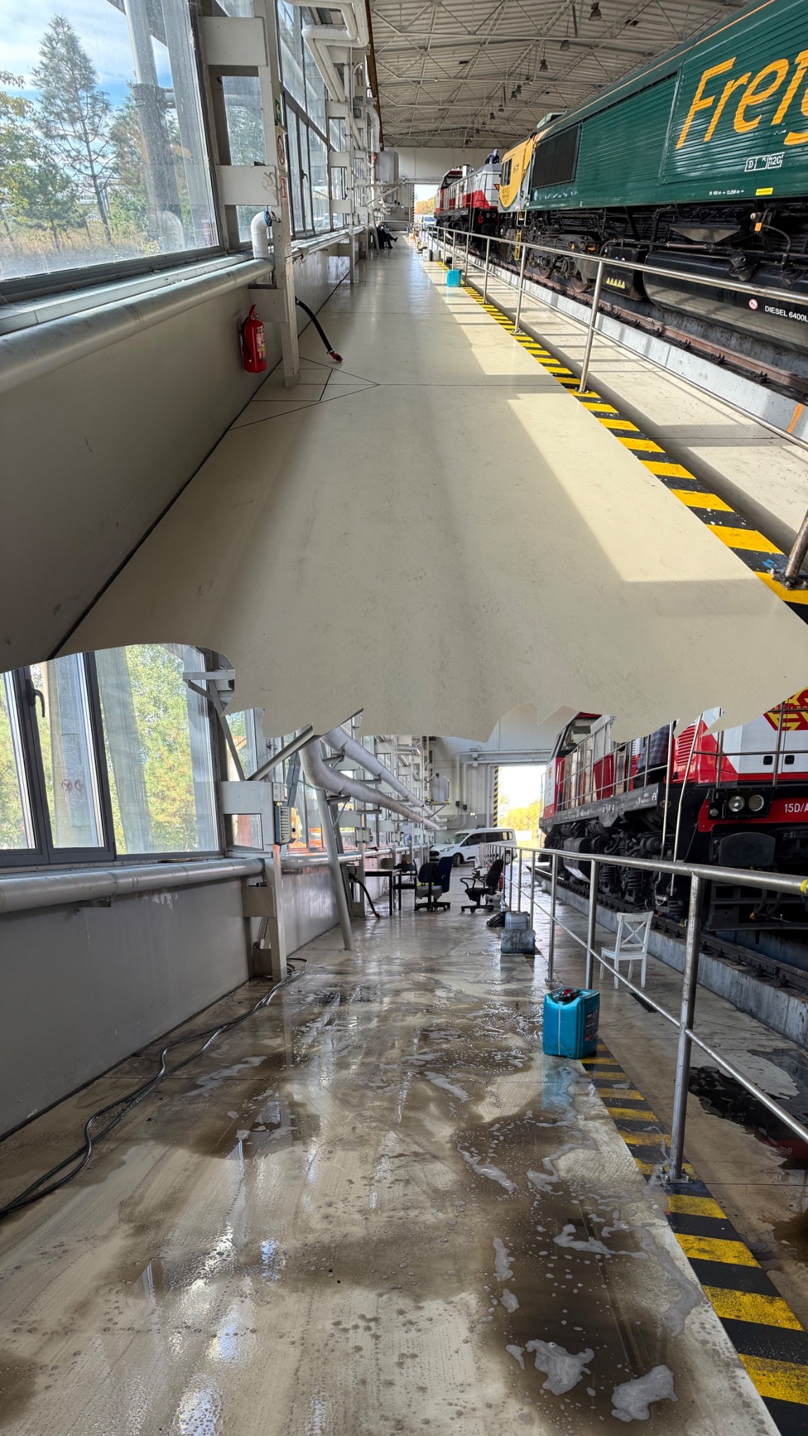 Przed i po myciu podłogi w hali z lokomotywami. Widoczne zabrudzenia i piana po czyszczeniu. W tle okna i elementy konstrukcji hali.