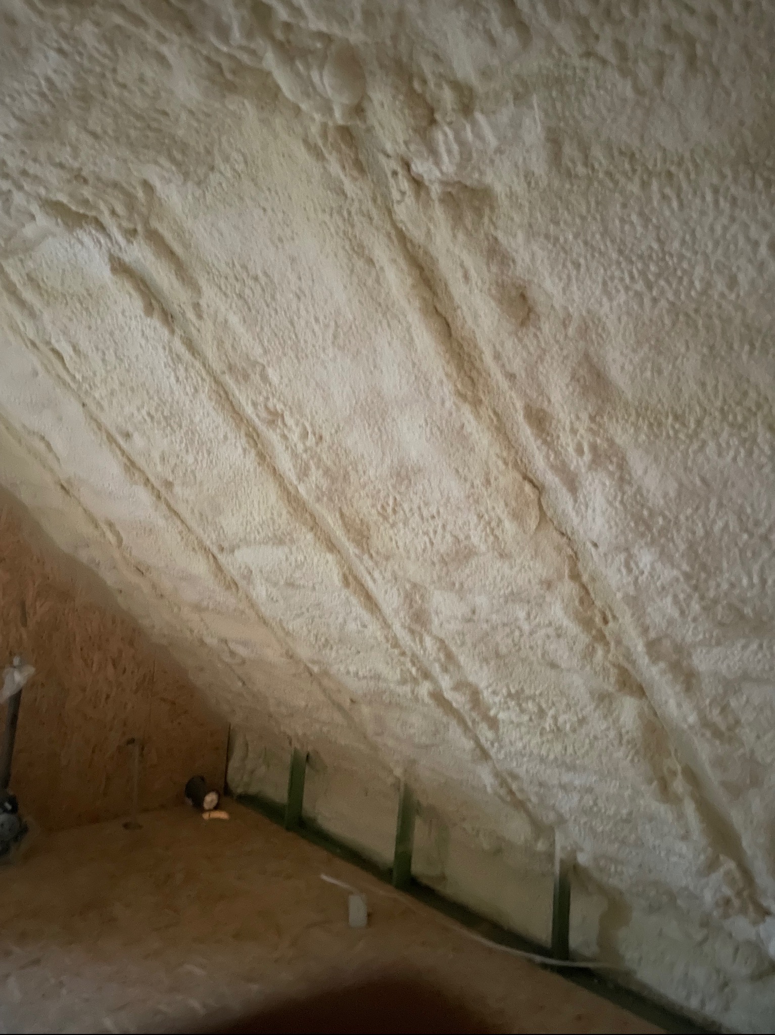 Poddasze ocieplone pianką poliuretanową, widoczne drewniane elementy konstrukcyjne i nierównomierna faktura izolacji.