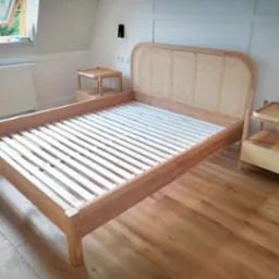 Rama łóżka z drewna z zagłówkiem z plecionki rattanowej, dopasowane szafki nocne z drewna, jasna podłoga, białe ściany i okno dachowe