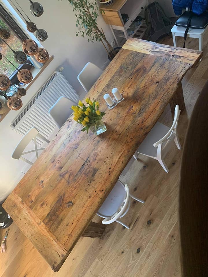 Rustykalny stół z litego drewna z nieregularnymi krawędziami, otoczony białymi krzesłami, na drewnianej podłodze, z bukietem żółtych tulipanów w wazonie i solniczką z pieprzniczką na blacie, widok...