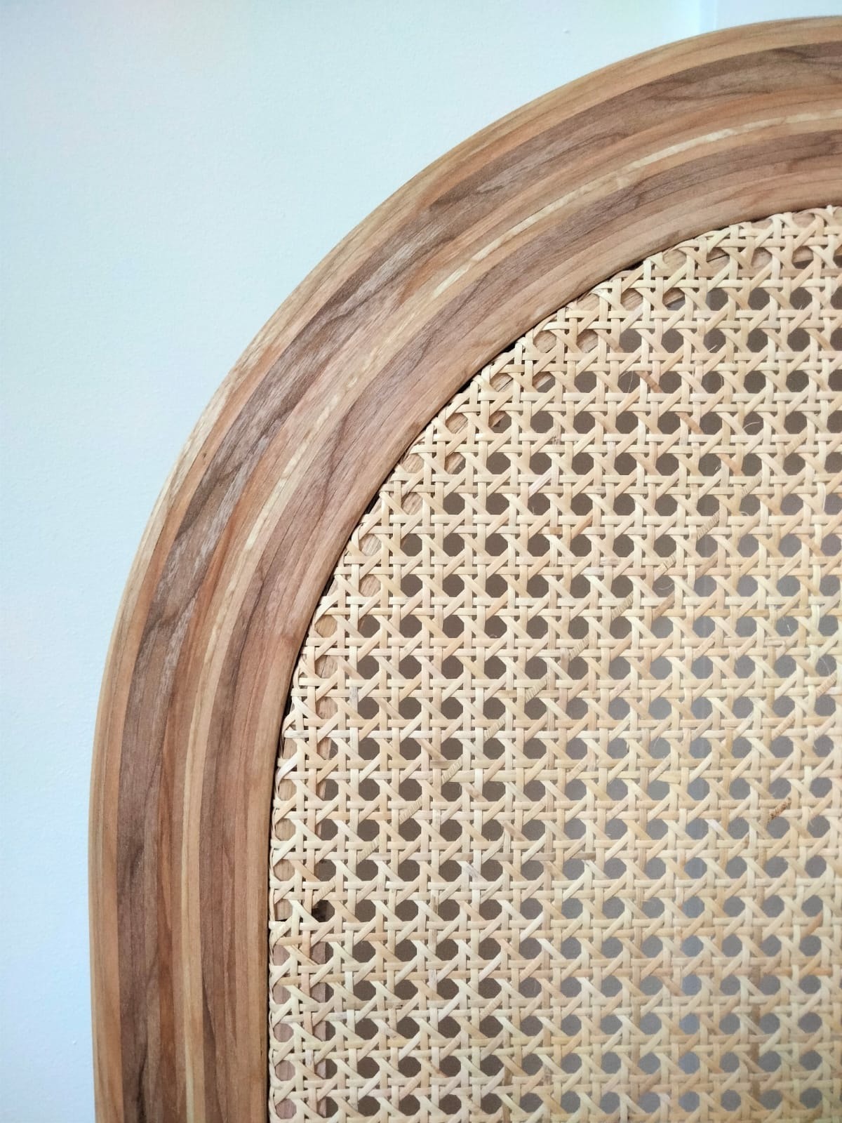 Fragment krzesła z drewnianą ramą o wyraźnym usłojeniu i rattanowym siedziskiem w regularny wzór.