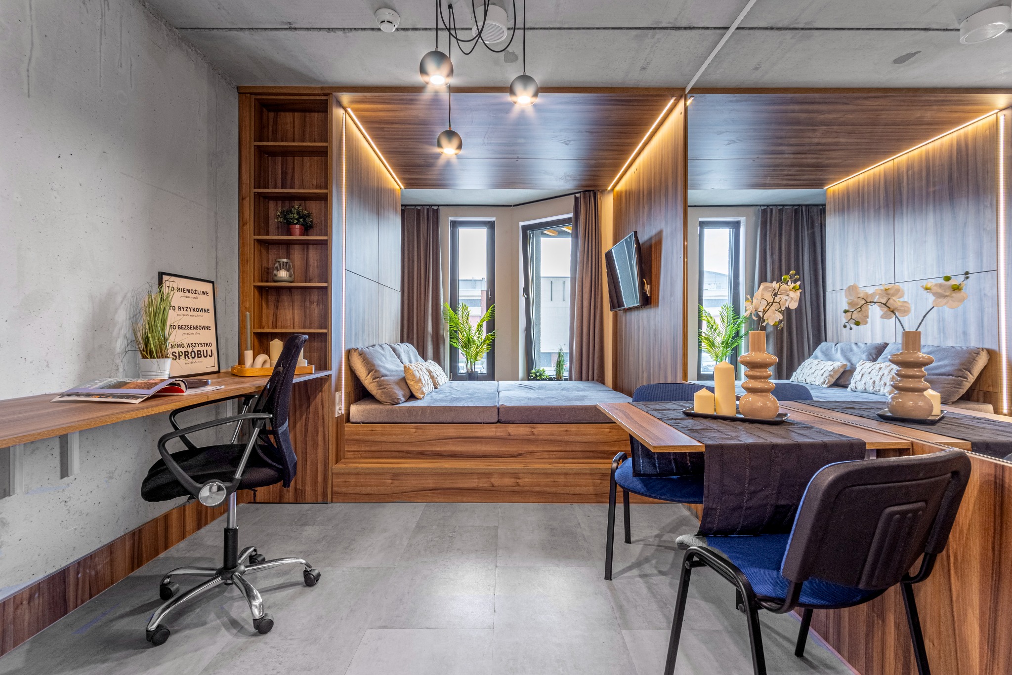 Nowoczesne wnętrze mieszkania z drewnianą zabudową, biurkiem i miejscem do spania wnęce, oświetlone taśmami LED, z szarą podłogą i betonową ścianą.