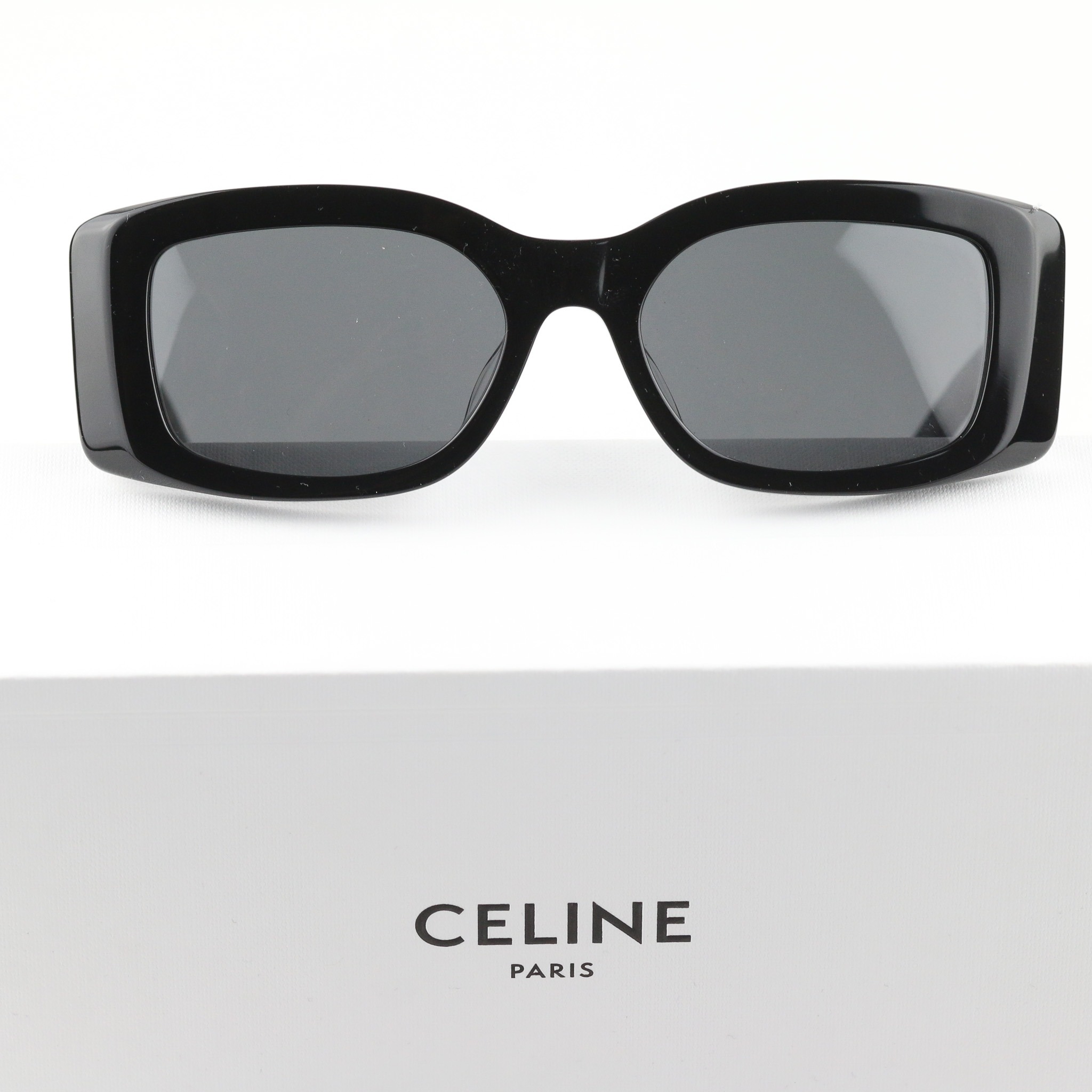 Czarne, masywne okulary przeciwsłoneczne Celine na białym pudełku z logo Celine Paris, widok z przodu, ostre światło.