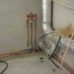 Miedziane rury instalacji wodnej wystające ze ściany, widoczne również rury wentylacyjne w surowym pomieszczeniu.