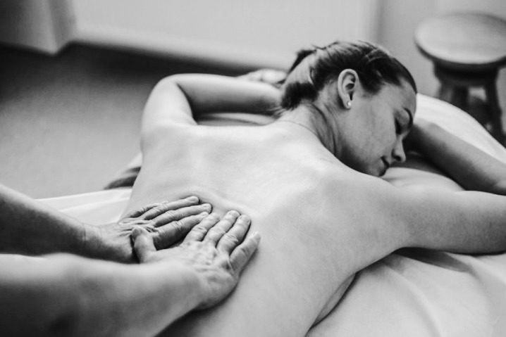 Czarno-białe zdjęcie z masażu pleców kobiety leżącej na stole do masażu, dłonie masażysty wykonują ruchy masujące.