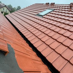 ARCHIQUALITY Krystian Nowak - Czerwona dachówka ceramiczna z oknem dachowym, widok z góry, fragment membrany dachowej widoczny z lewej strony.