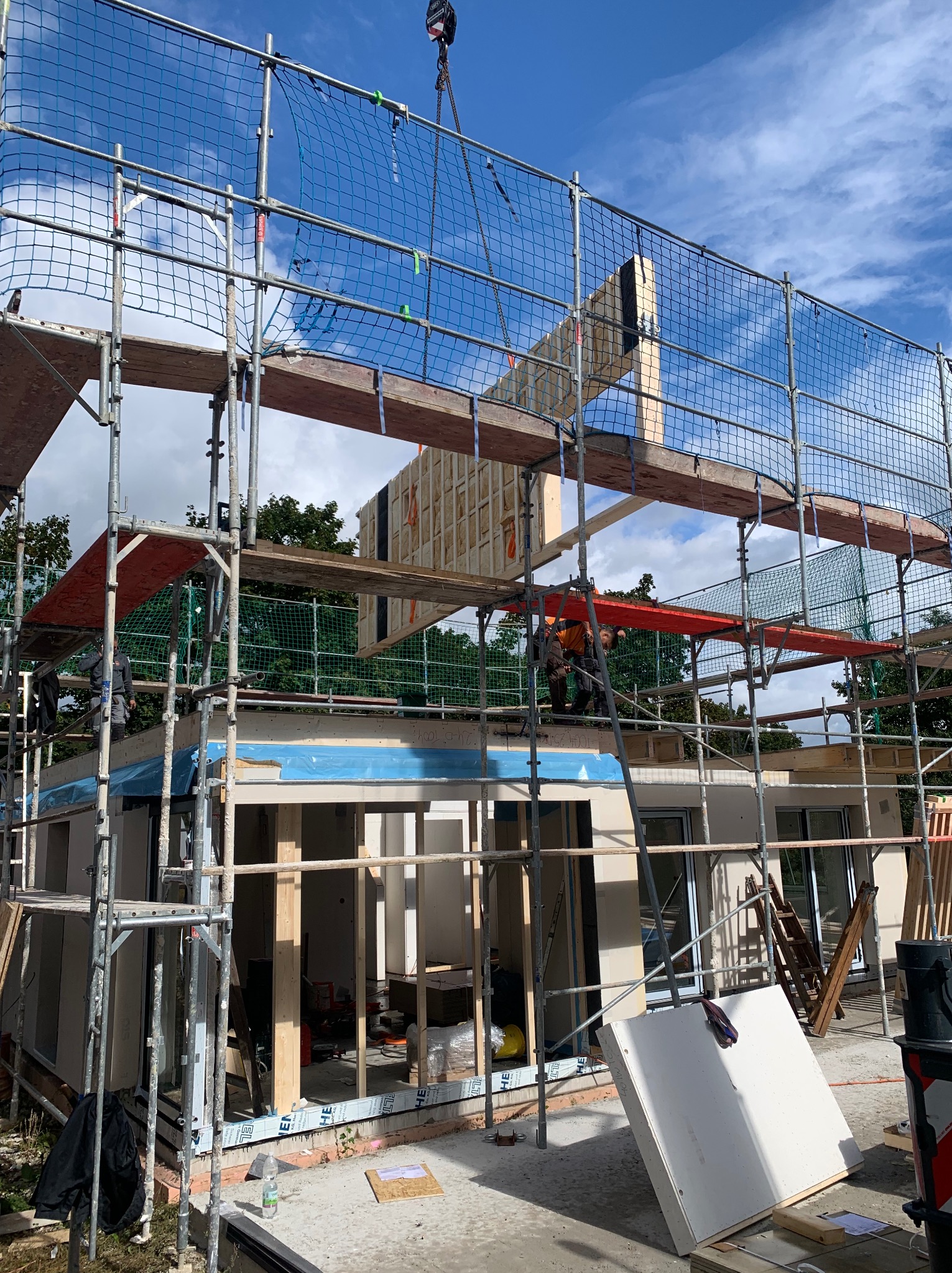 Montaż ściany domu szkieletowego w Dębnie przy użyciu dźwigu, widoczne rusztowania i pracownicy budowlani.