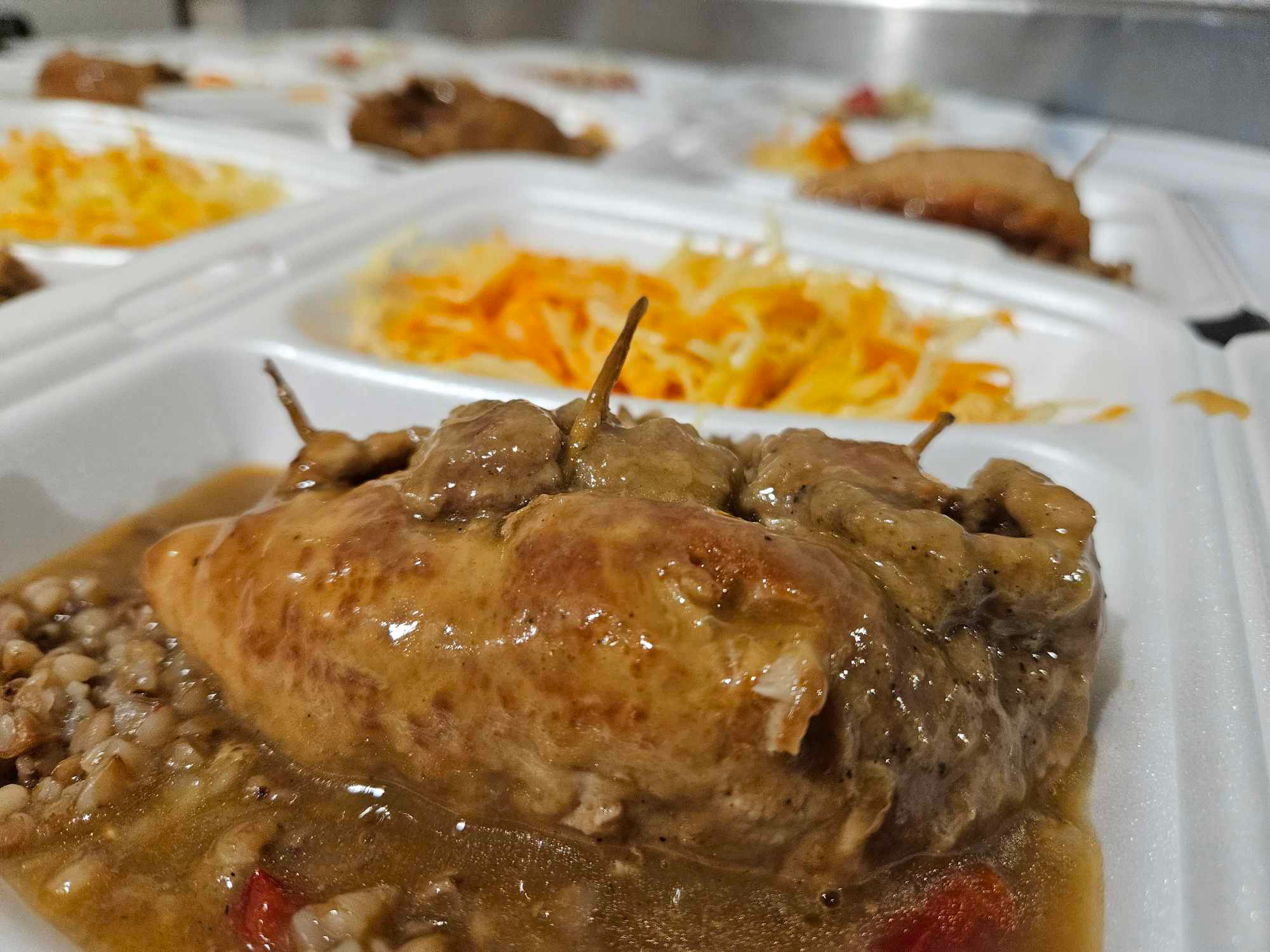 Porcja obiadowa w styropianowym pojemniku: duszona pierś kurczaka w sosie, kasza gryczana i surówka z marchewki.