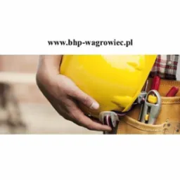 Pracownik z narzędziami i żółtym kaskiem w Wągrowcu, w tle ceglana ściana i adres strony internetowej.