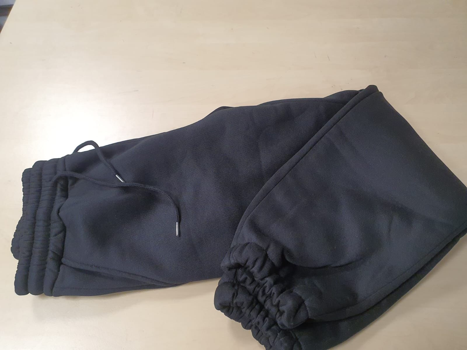Ciemne, dresowe spodnie ze ściągaczami na nogawkach i sznurkiem w pasie, leżące na jasnym blacie.