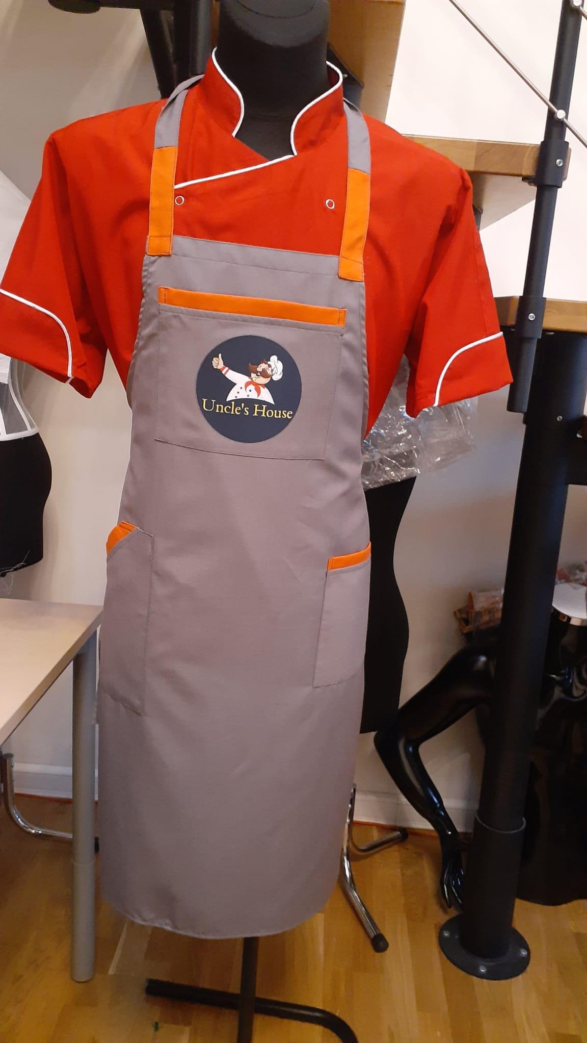 Czerwona bluza kucharska i szary fartuch z logo 'Uncle's House' na manekinie, widoczne kieszenie z pomarańczowymi detalami.