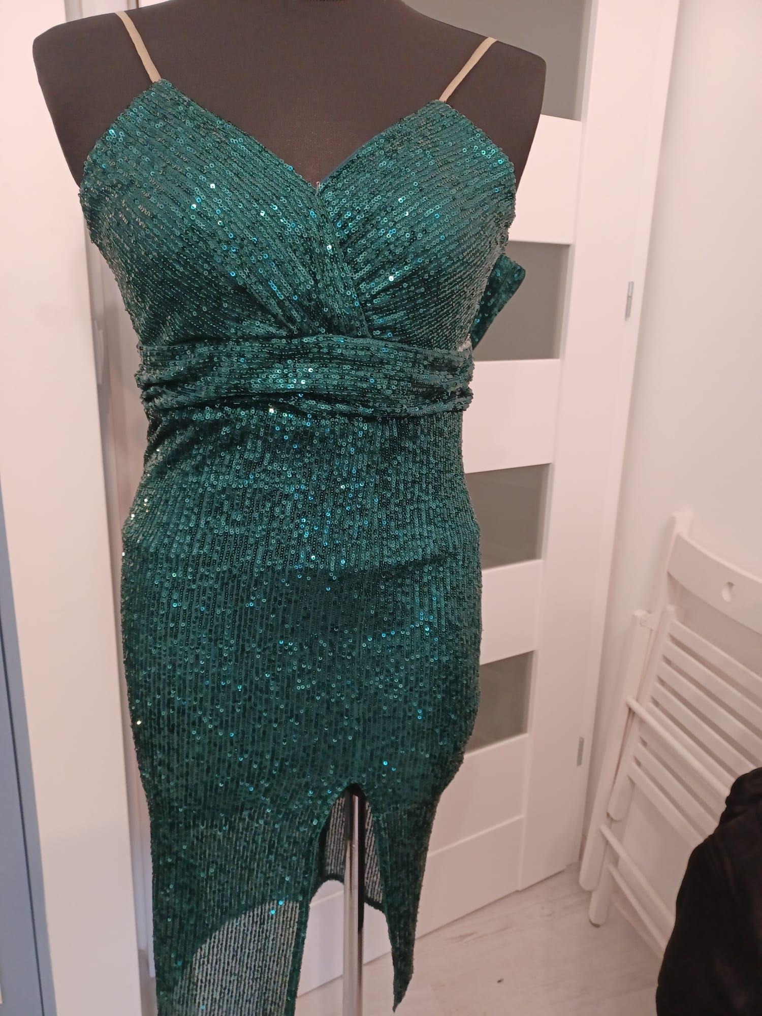 Emerald green sequined dress with spaghetti straps and a high slit, displayed on a mannequin against a white door with frosted glass panels.