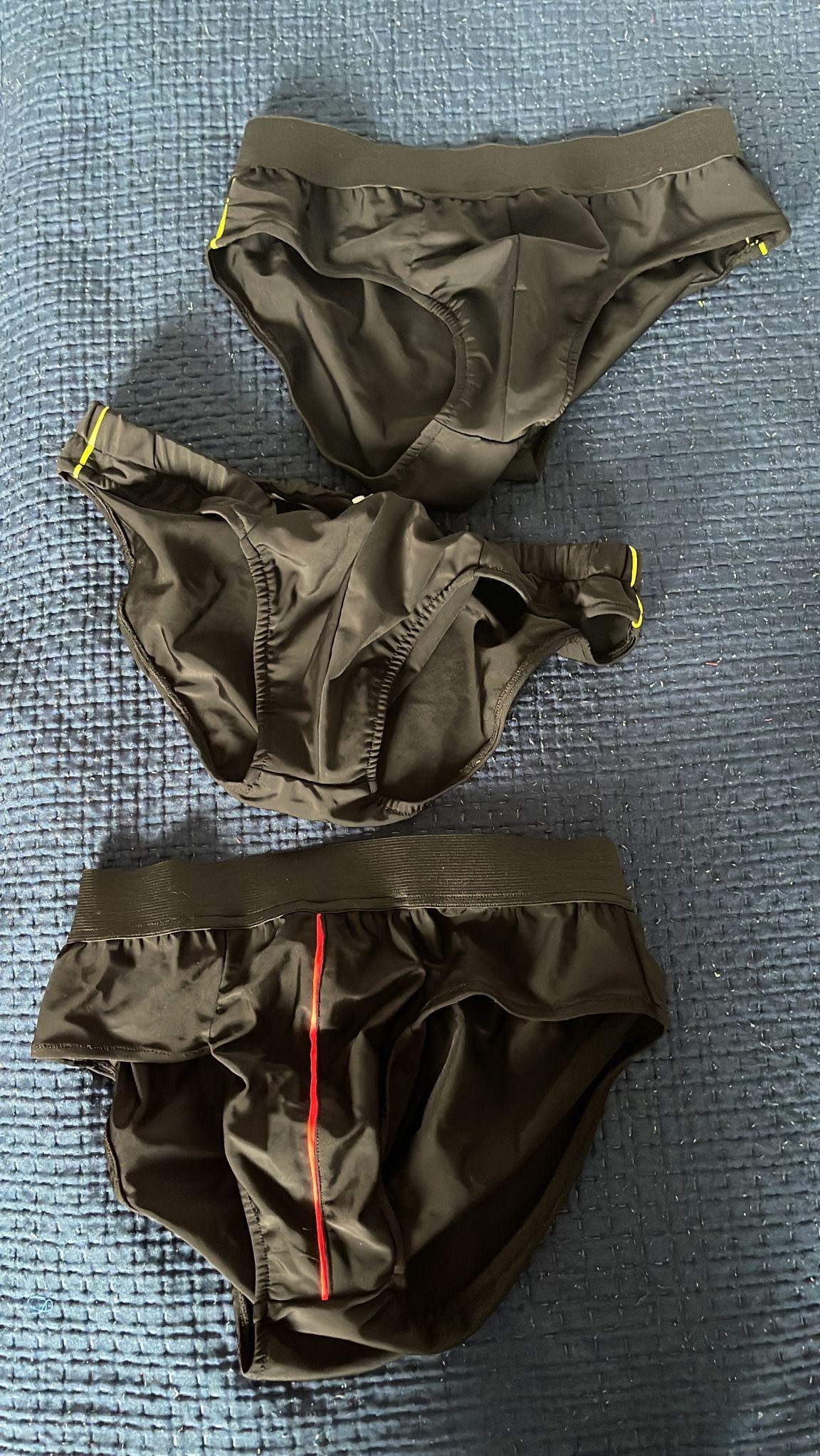 Trzy pary czarnych, męskich slipów na niebieskiej, pikowanej narzucie. Jedne z żółtymi detalami, drugie z czerwoną linią.