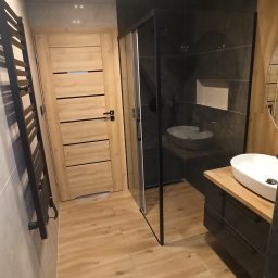 Paweł Pielak - Nowoczesna łazienka z drewnianymi akcentami, kabiną prysznicową typu walk-in, grzejnikiem drabinkowym i drewnopodobną podłogą.