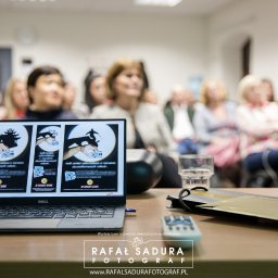 RafalSaduraFotograf.pl - Laptop wyświetlający grafiki z motywem teatru cieni i logotypem banku, widoczny na tle publiczności podczas prezentacji.