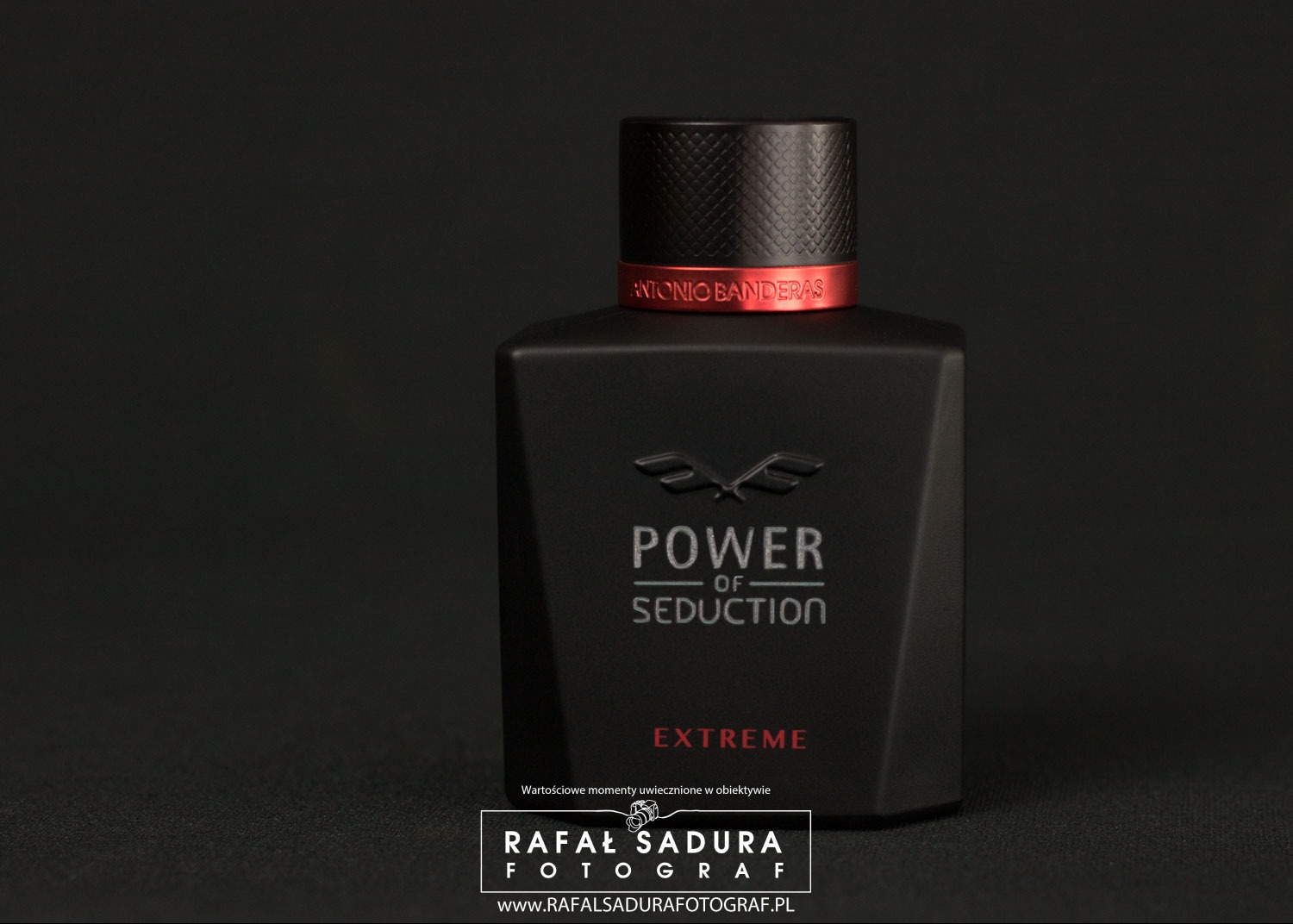 Czarne, matowe opakowanie perfum Antonio Banderas Power of Seduction Extreme na ciemnym tle, z czerwonym akcentem na szyjce flakonu i subtelnym oświetleniem podkreślającym logo fotografa w dolnej...