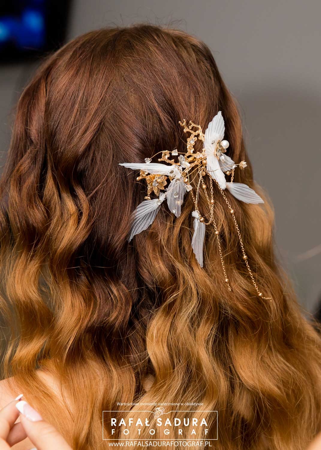Upięcie ślubne: brązowe włosy z delikatną ozdobą z białych piórek, złotych gałązek i łańcuszków.
