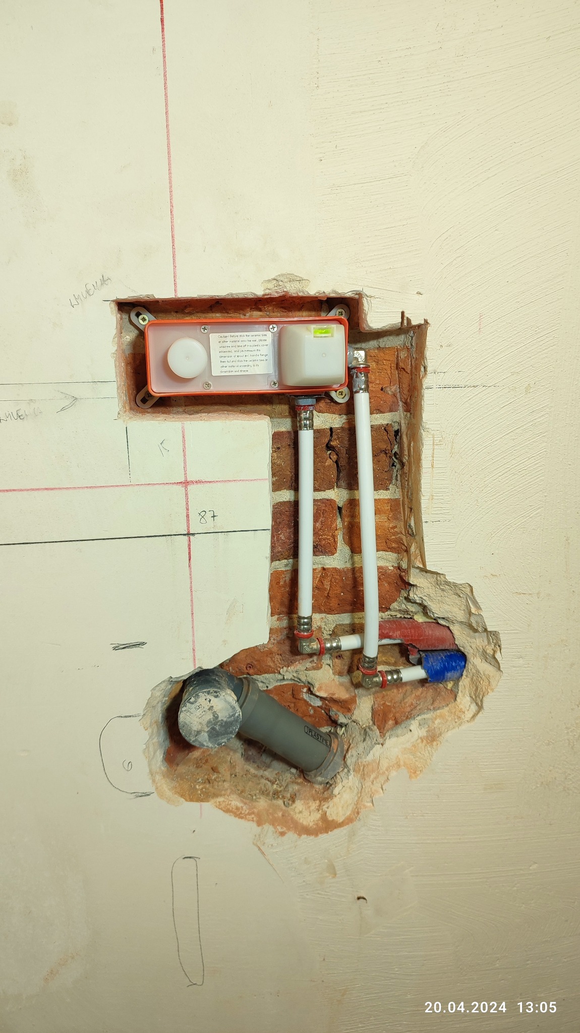 Widok na fragment ściany z widoczną instalacją podtynkową do WC w trakcie montażu, z widocznymi rurami doprowadzającymi wodę, odpływem kanalizacyjnym oraz elementami montażowymi osadzonymi w murze...