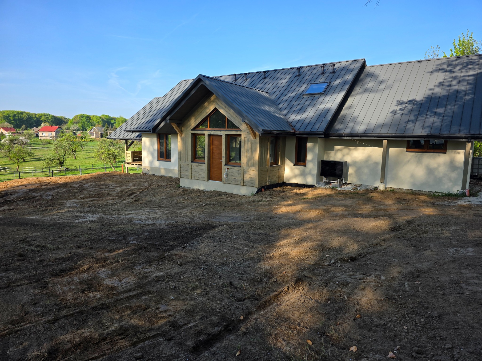 Nowoczesny dom szkieletowy z grafitowym dachem w Krakowie, widok z zewnątrz na tle zieleni. Dom z drewnianymi elementami wykończeniowymi.