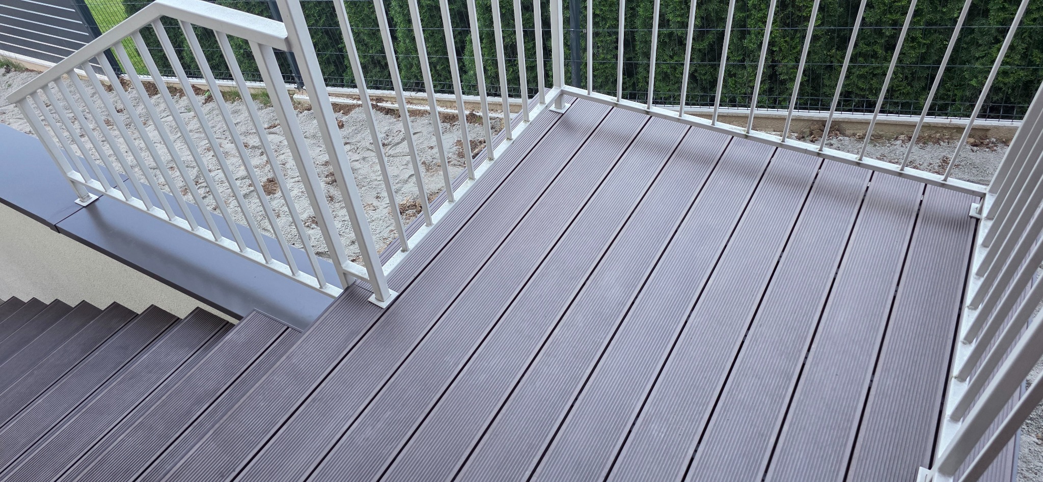 Nowoczesny taras kompozytowy z szarych desek, biała balustrada, widok z góry na schody. Estetyczne wykończenie zewnętrzne z dbałością o szczegóły.