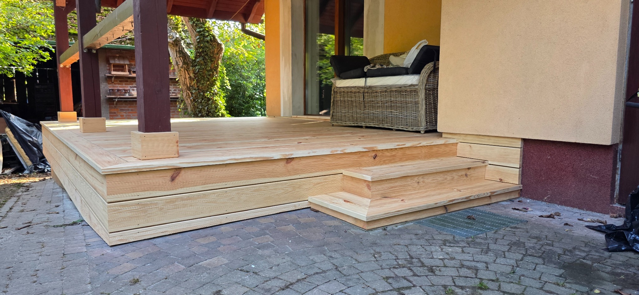 Nowy taras z drewna, z niskimi schodkami, z krzesłem na górze, Kraków. Jasne drewno, widoczne słoje, schludne wykonanie, kostka brukowa dookoła.