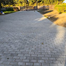 Zenith-Bruk - Szara kostka brukowa ułożona na podjeździe, w tle widoczny fragment ogrodzenia i zaparkowany samochód dostawczy.