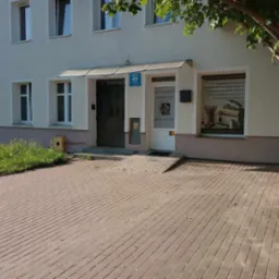 Wejście do biura rachunkowego z rampą dla niepełnosprawnych, tabliczka z numerem 49 i informacją o godzinach otwarcia, reklama na szybie z ofertą usług księgowych i adresem strony internetowej.