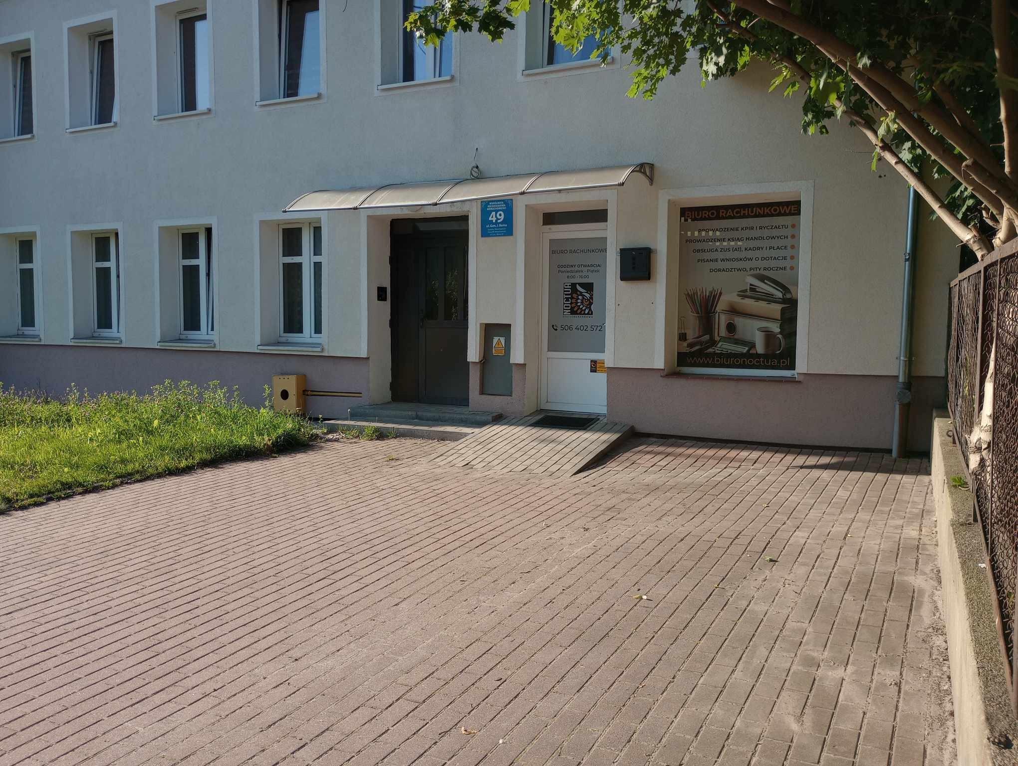 Wejście do biura rachunkowego z rampą dla niepełnosprawnych, tabliczka z numerem 49 i informacją o godzinach otwarcia, reklama na szybie z ofertą usług księgowych i adresem strony internetowej.
