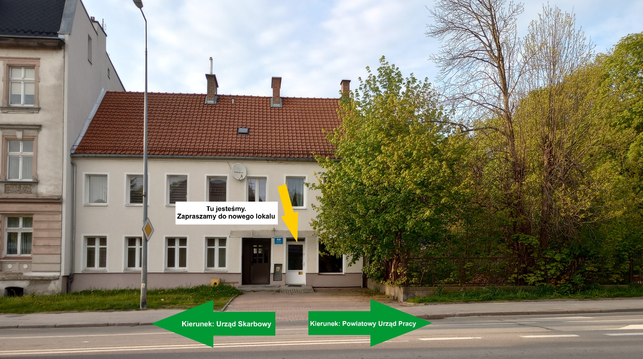 Fasada budynku z napisem 'Tu jesteśmy. Zapraszamy do nowego lokalu' nad wejściem, strzałki wskazujące kierunek do Urzędu Skarbowego i Powiatowego Urzędu Pracy.