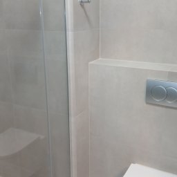 Kamil Pawłowski - Minimalistyczna łazienka po remoncie: kabina prysznicowa ze szklanymi drzwiami, podwieszana toaleta i beżowe płytki tworzą spójną, nowoczesną przestrzeń.