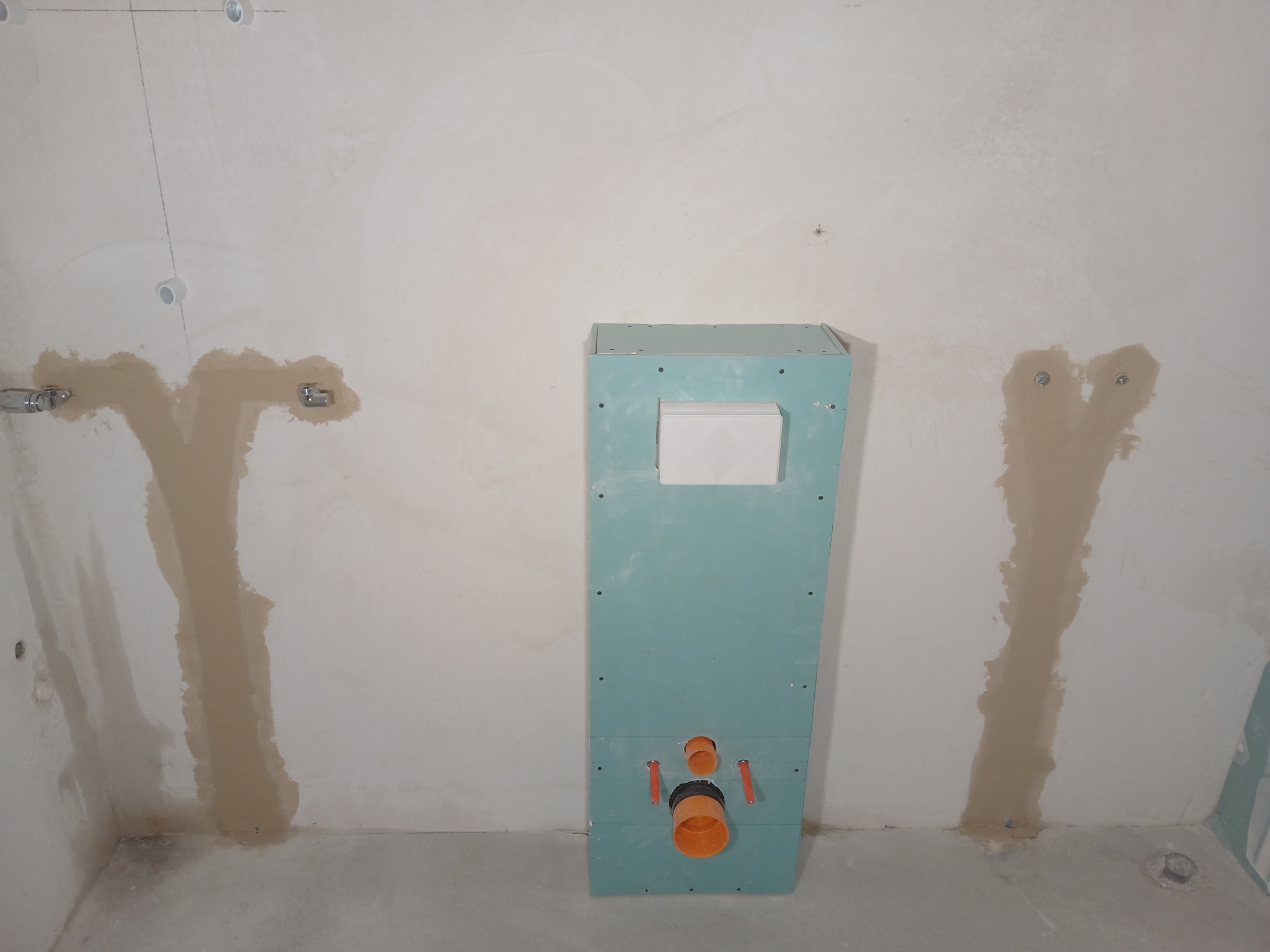 Stelaż podtynkowy do WC zamontowany na ścianie w trakcie prac wykończeniowych, widoczne przyłącza kanalizacyjne i ślady po szpachlowaniu.