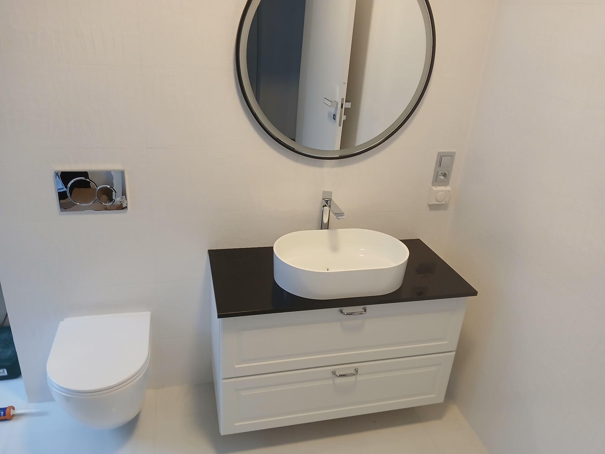 Nowoczesna łazienka z podwieszaną toaletą, owalną umywalką nablatową na czarnym blacie, lustrem z podświetleniem LED oraz minimalistyczną armaturą.